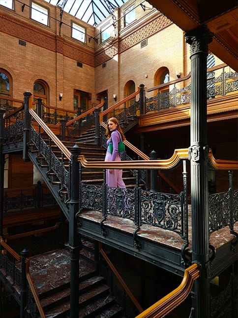 A high resolution photo of a woman standing in a brick atrium with multiple floors of stairs with …