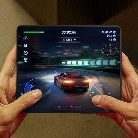 Hands holding an unfolded Galaxy Z Fold4. The Main Screen displays a scene from a racing game. A …