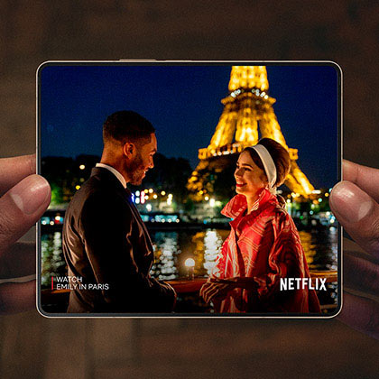 Hands holding an unfolded Galaxy Z Fold4. The Main Screen displays a scene from a Netflix video …