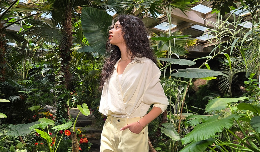 A woman stands with plants surrounding her. With Super HDR, appropriate lighting adjustments are applied to the photo.