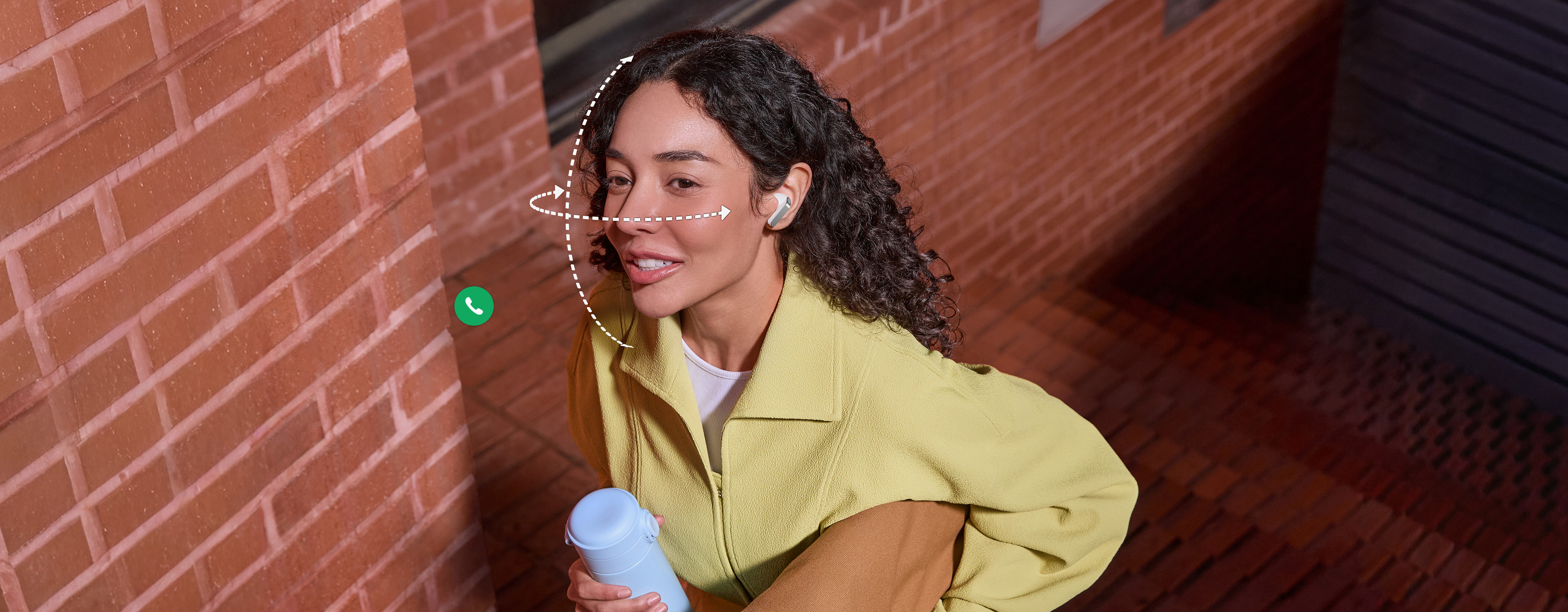 A person wearing Galaxy Buds4 Pro in White, while holding a tumbler in one hand and a bag in the other. Dotted vertical and horizontal lines wrap around her face to show the Head Gesture function available on the Galaxy Buds4 Pro. Call app icon and Bixby icon indicates the two features can be used for Head Gesture.