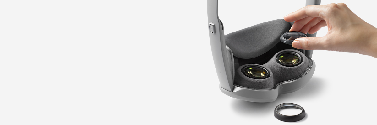 Galaxy XR is placed vertically facing down and a person is placing a prescription optical lens on the right lens on the inside of the device. Another prescription lens is placed next to the device.